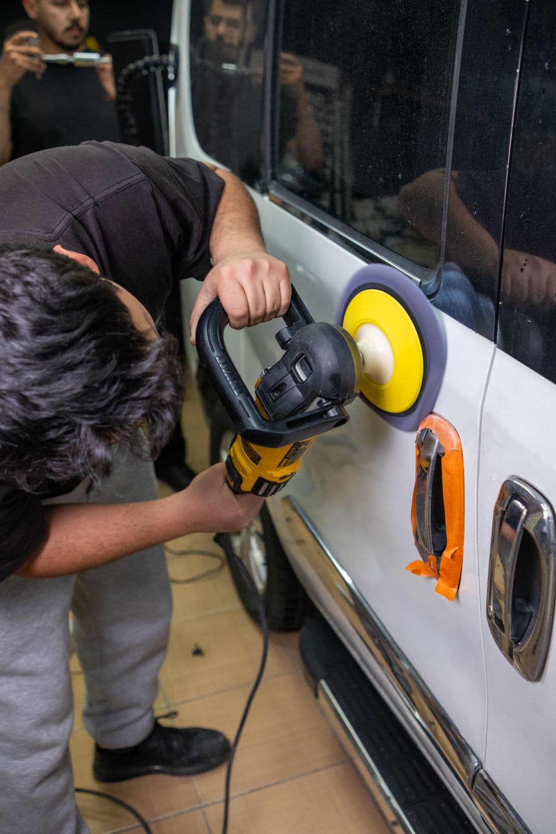 Professional detailer polishing a car door with an electric buffer in a workshop