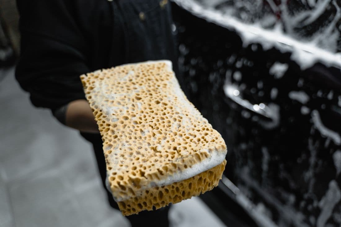 Person washing a car with a sponge covered in soap suds