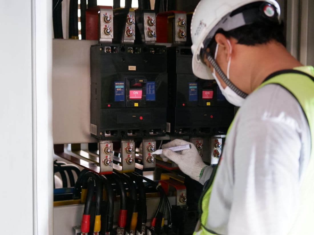 Technician in safety gear inspecting an electrical panel in an industrial setting