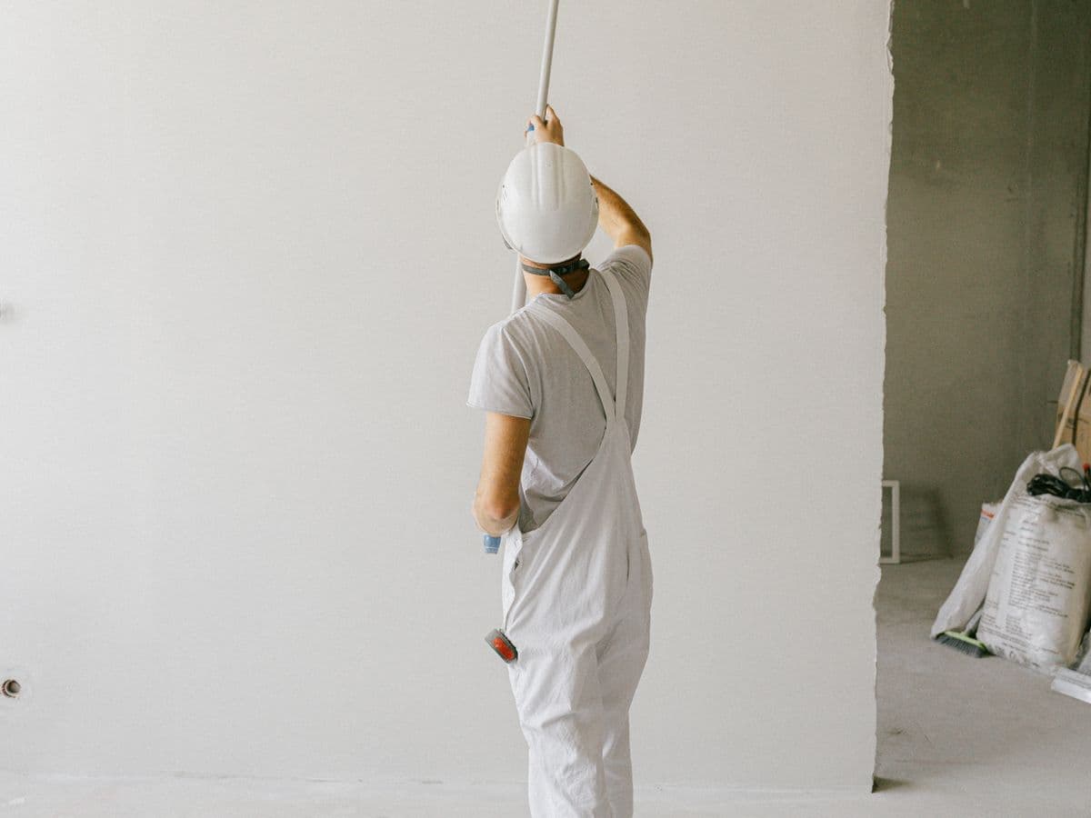 House painter in overalls rolling paint on an interior wall