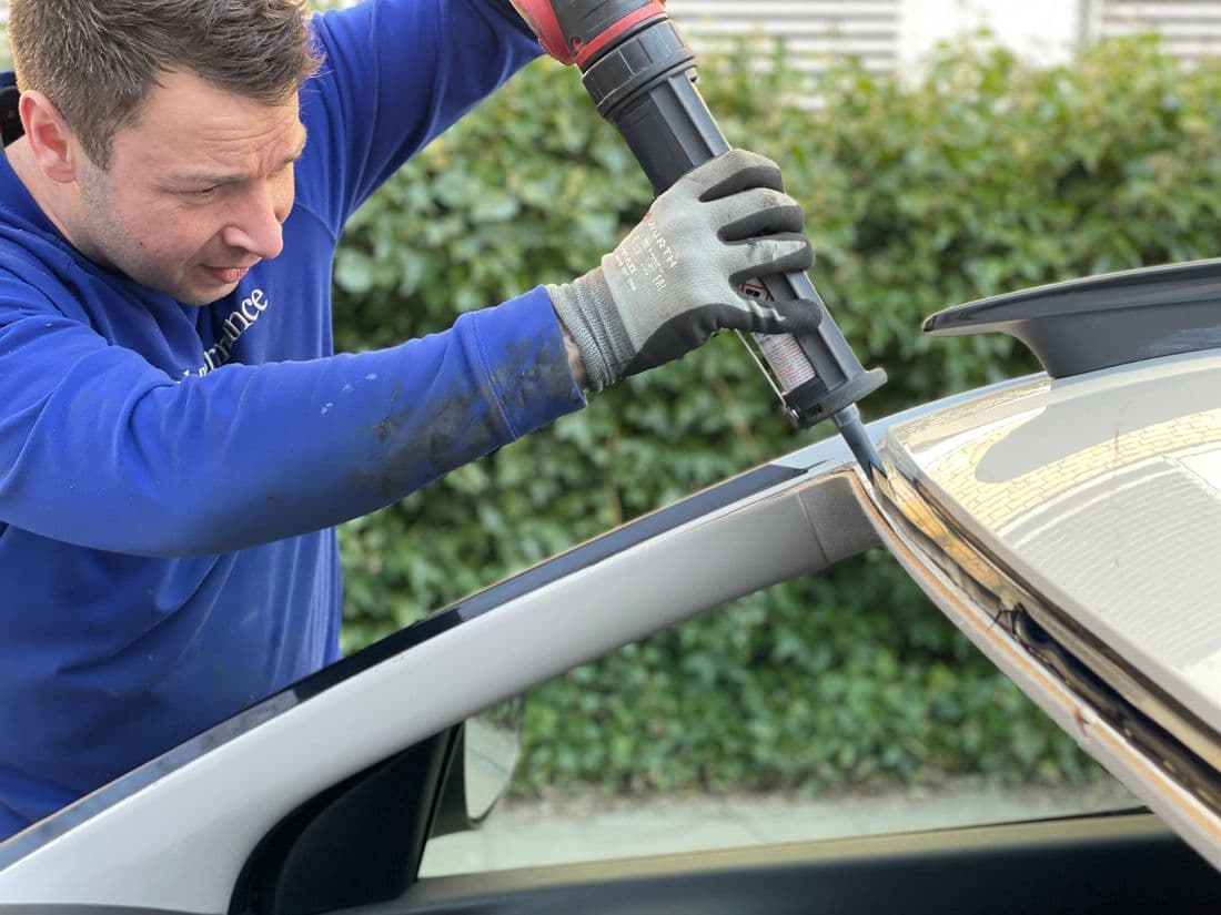 Auto glass technician applying windshield urethane sealant with a powered gun