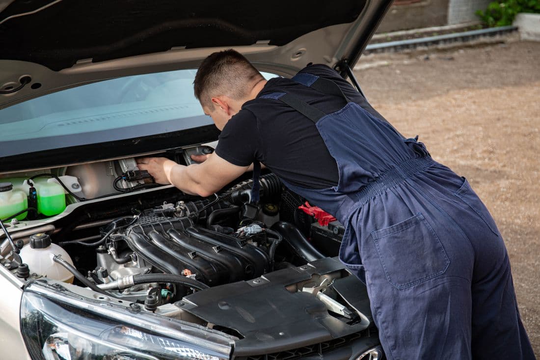 Mechanic in overalls fixing a car engine outdoors