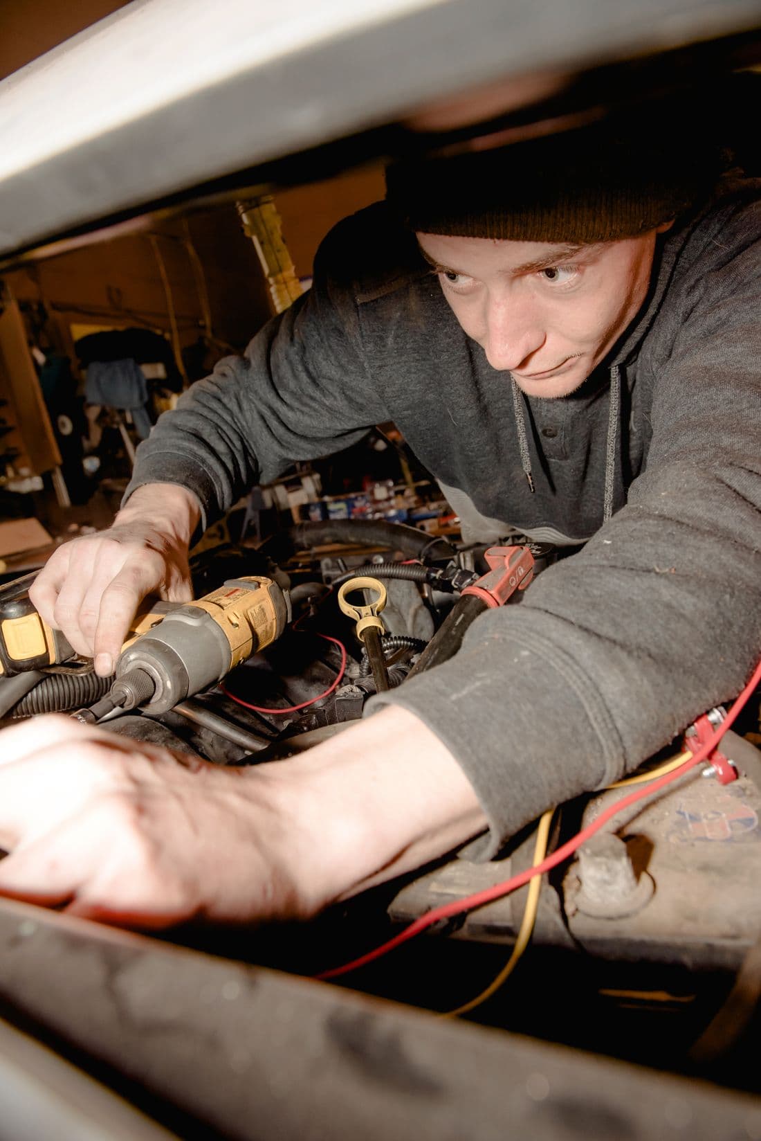 Mechanic repairing a car engine inside a garage using a power tool