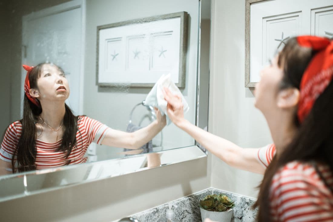 Woman wiping a bathroom mirror with a cleaning cloth