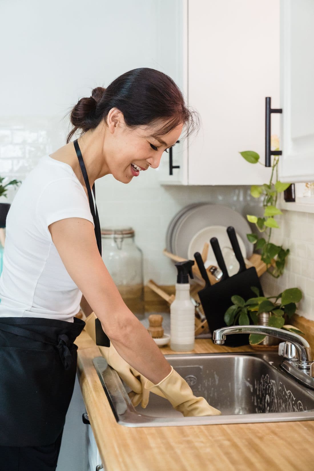 Smiling woman washing dishes with gloves in a kitchen sink area