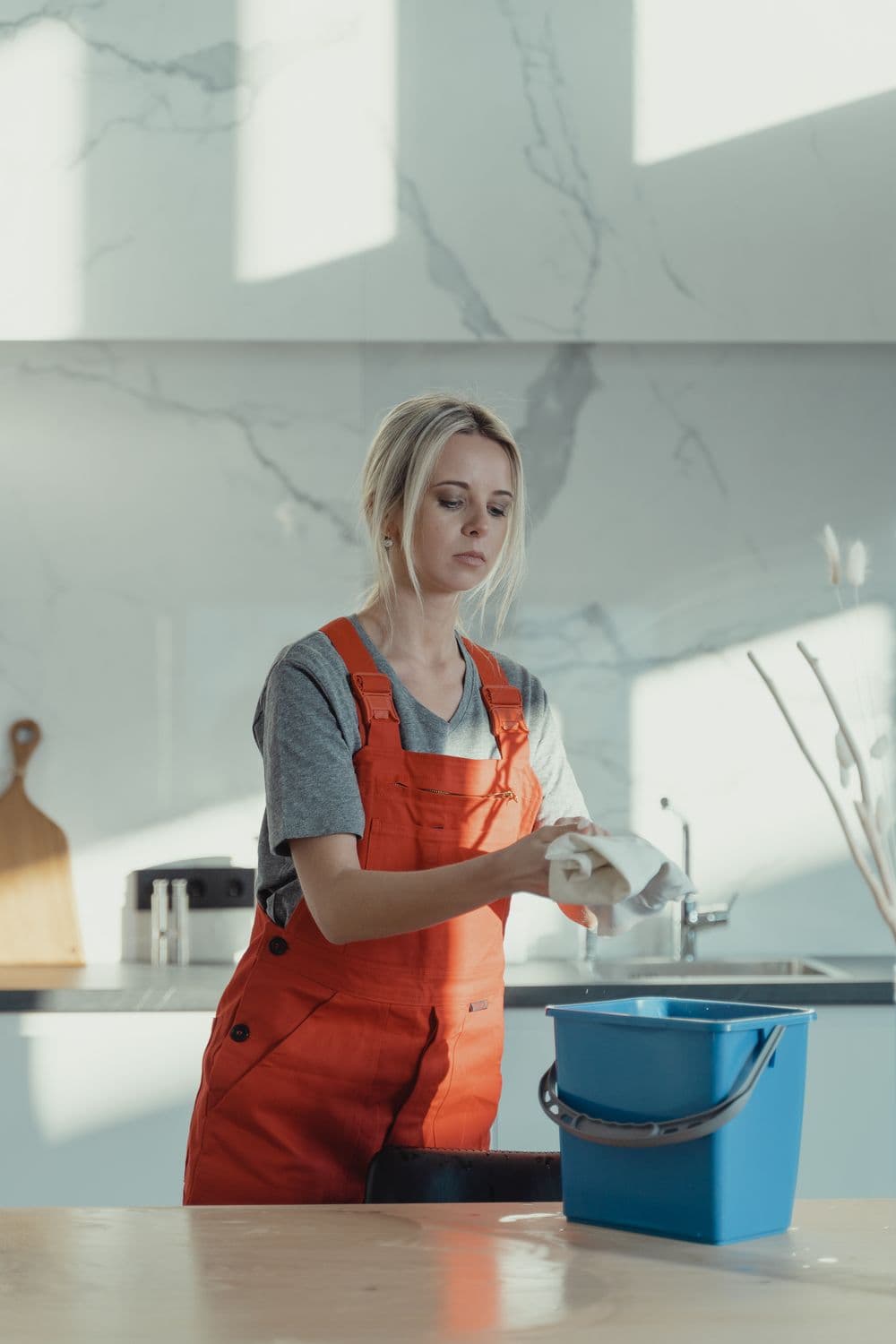 Professional cleaner in orange overalls sanitizing a kitchen table in a modern home