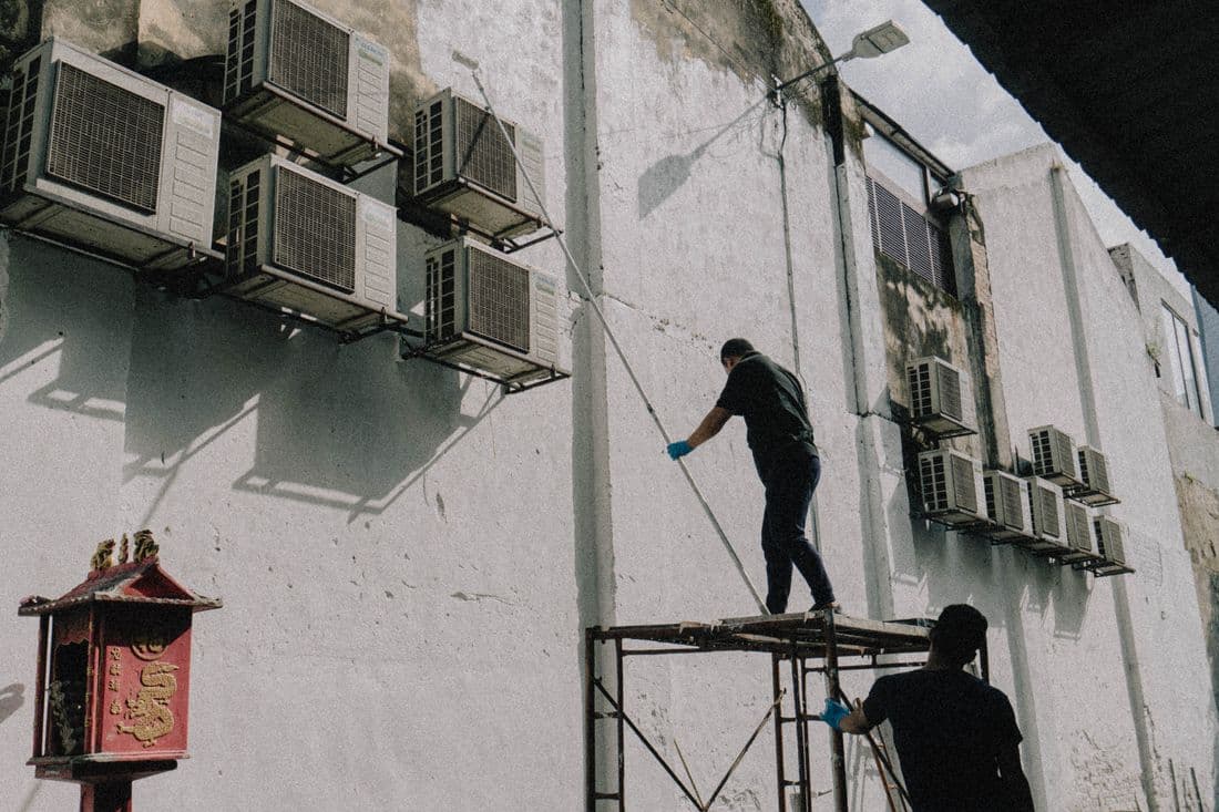 Workers on scaffold maintaining air conditioning units on a building exterior