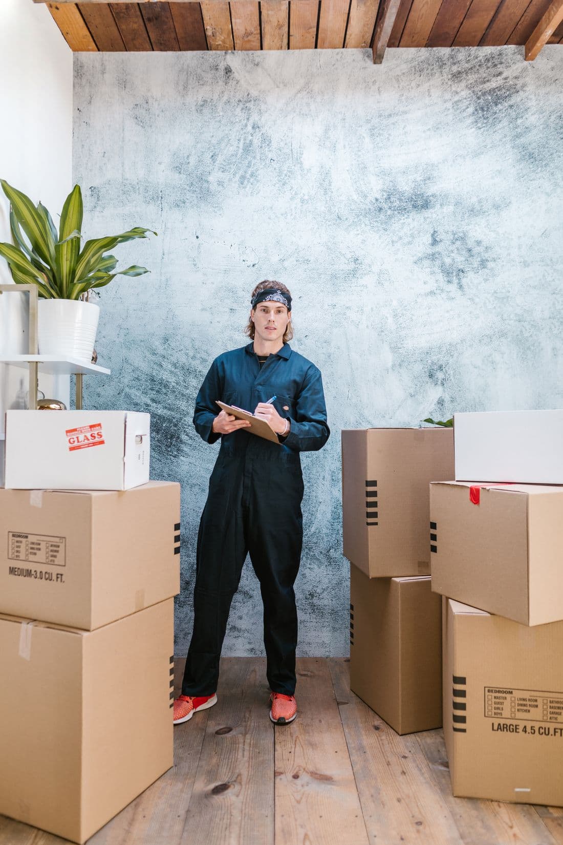 Professional mover in coveralls organizing packages with a clipboard on moving day