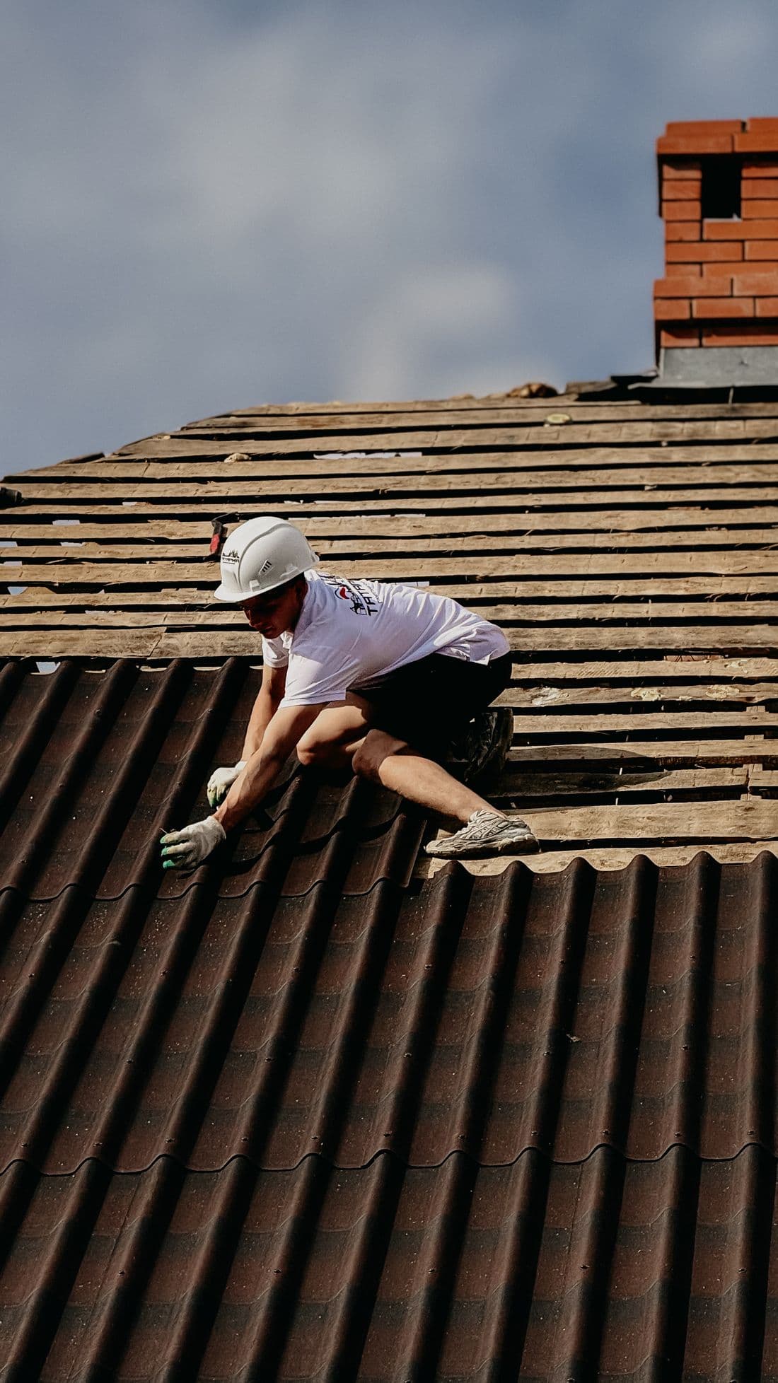 Roofer installing roofing tiles wearing protective safety gear on a sloped roof