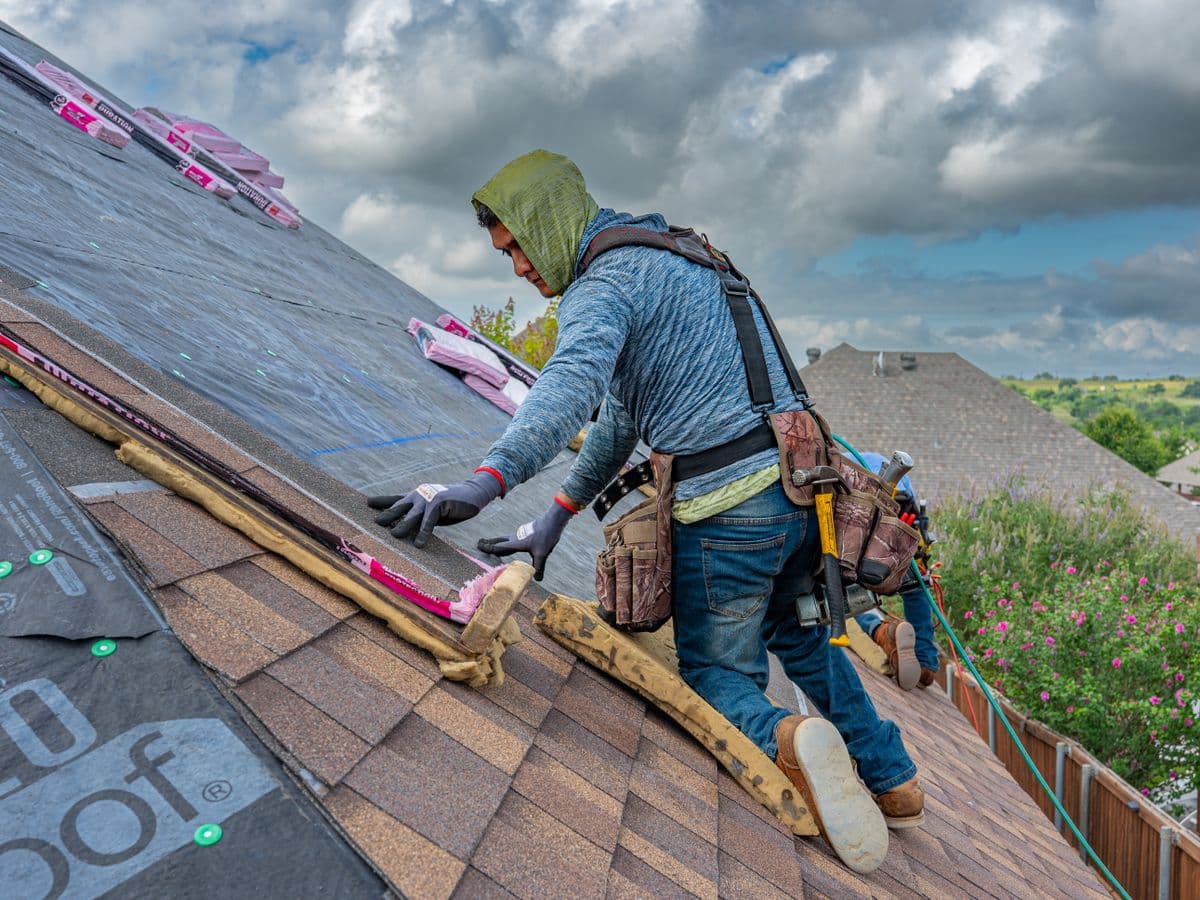 Roofer installing shingles on a home under blue skies